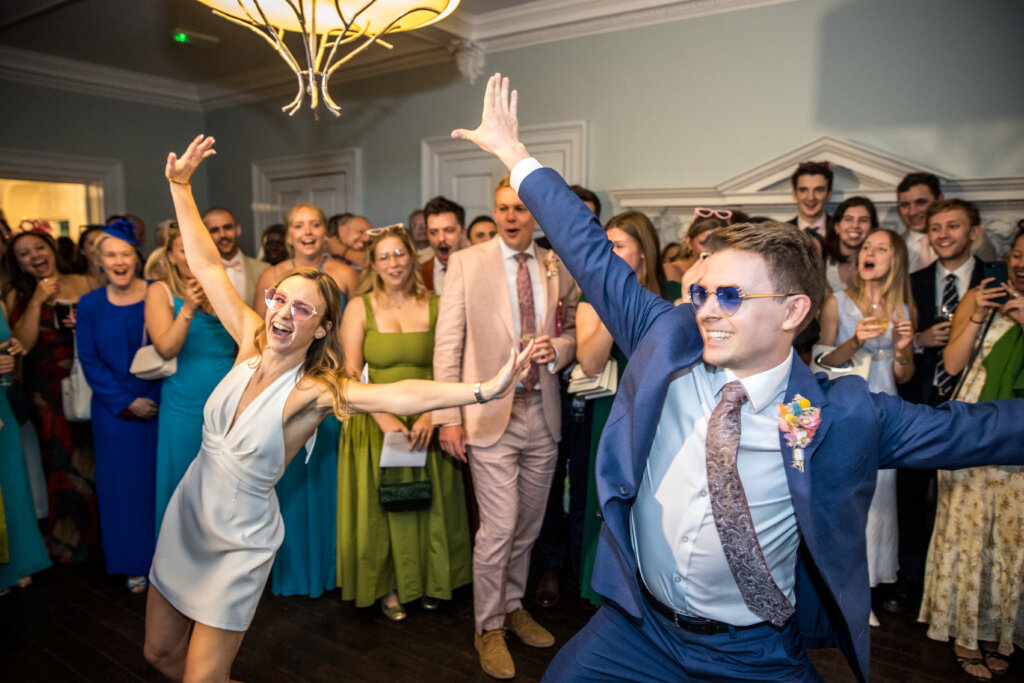 Bride and groom performing choreographed first dance with arms stretched out in Willow Room at Morden Hall