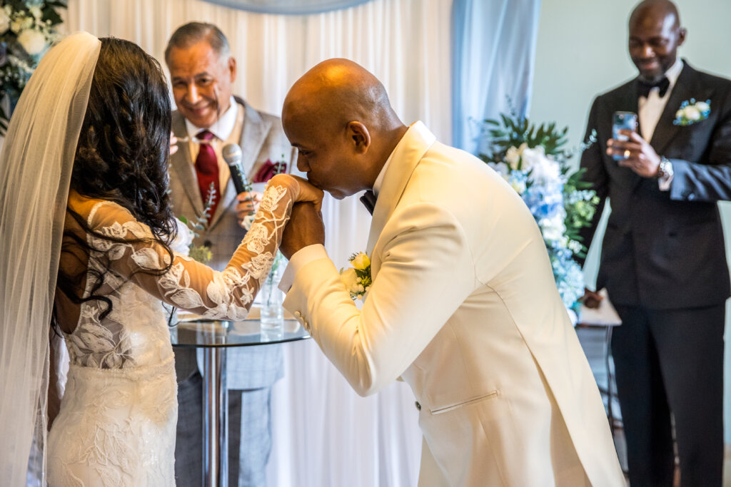 Groom kissing bride hand at the end of the ceremony in the Willow Room at Morden Hall