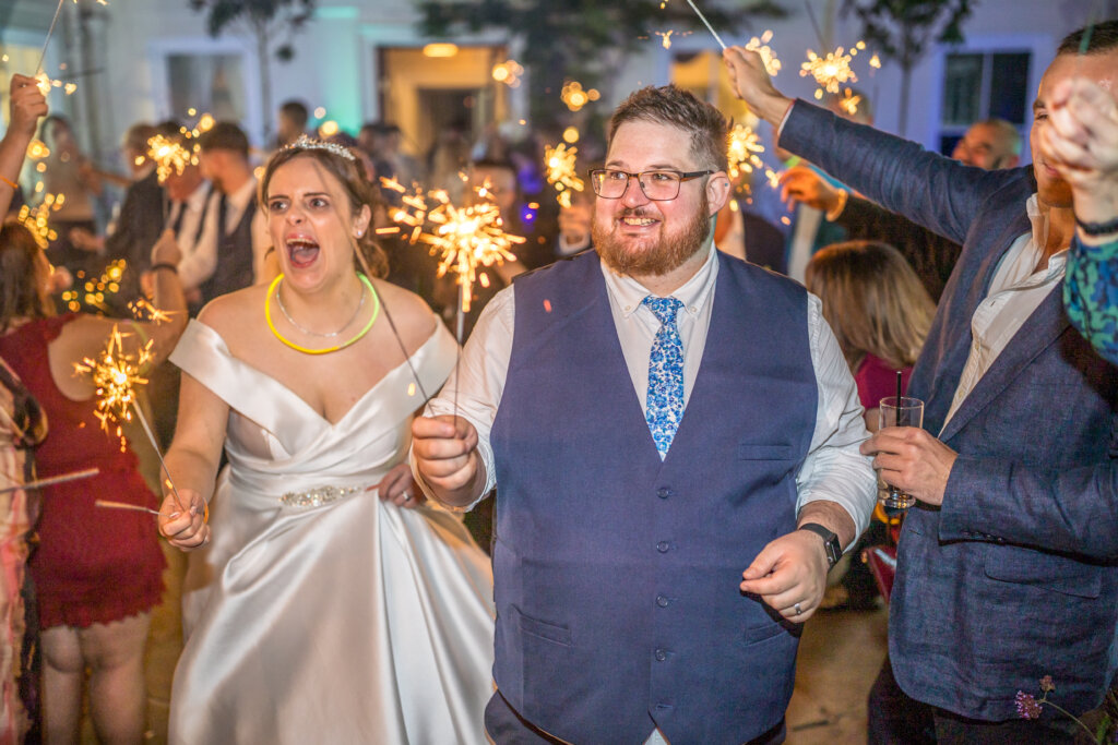 Bride and groom walking through sparklers held by guests at Morden Hall front entrance at night