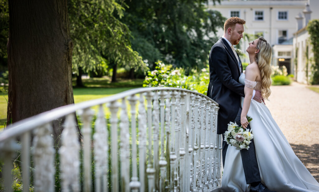 Bride and groom looking into each others eyes at the end of the bridge fence with Morden Hall in background