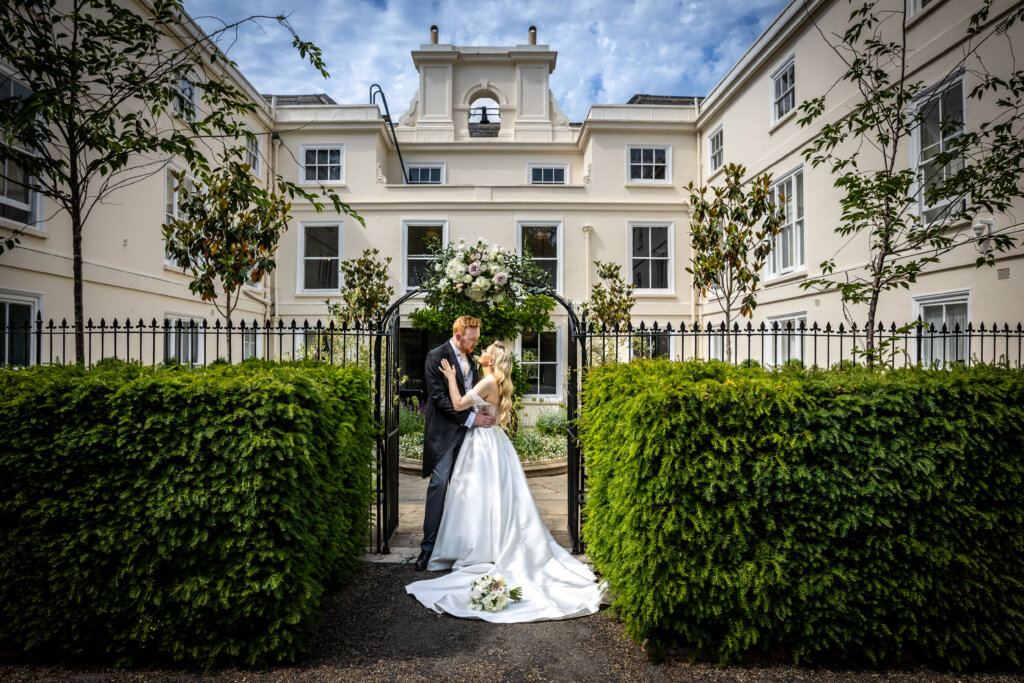 Bride and groom under the front entrance arch of Morden Hall with the bell and courtyard behind