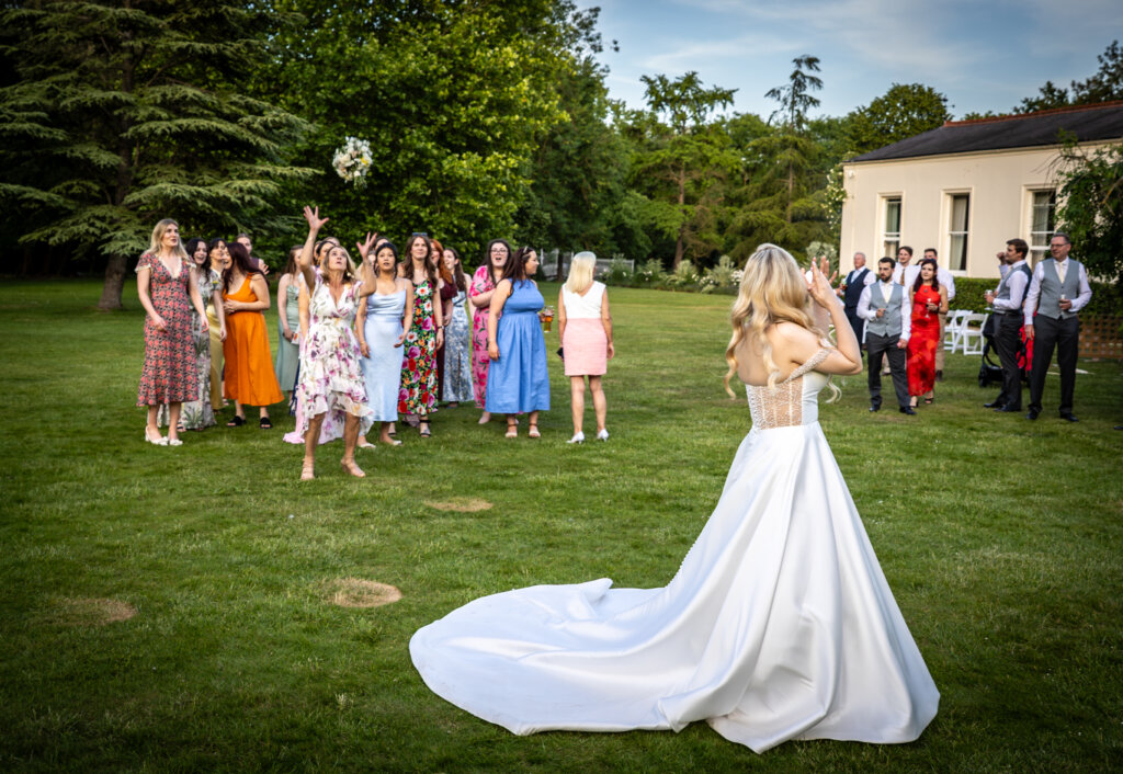 Bride tossing her wedding bouquet to guests on the lawn at Morden Hall