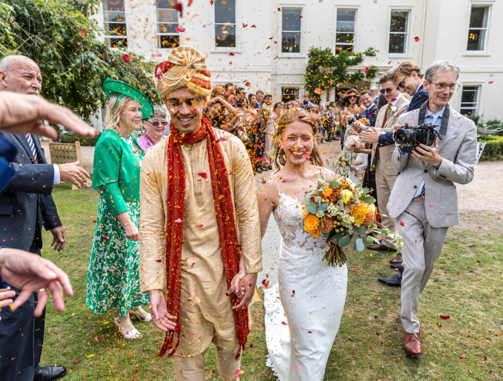 Bride and groom walking through confetti toss on the north lawn at Morden Hall