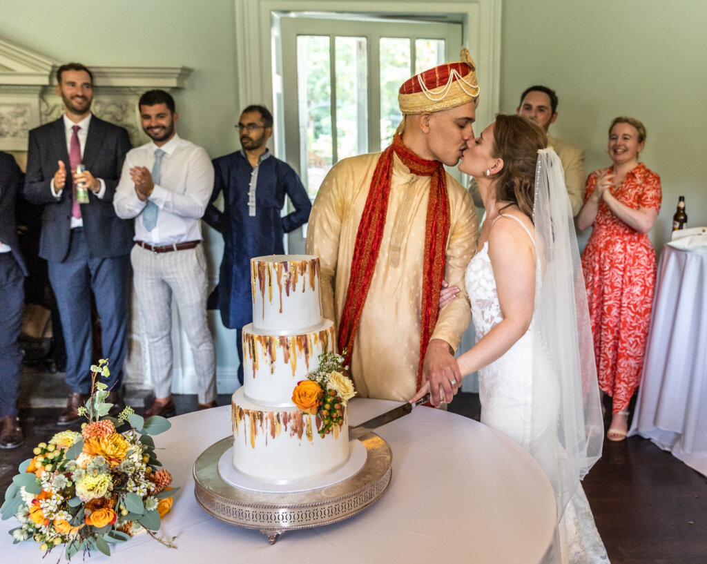Bride and groom kissing while cutting their wedding cake in Hawthorn Room at Morden Hall